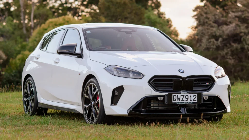 Front three-quarter view of a white BMW M135i parked on grass in a New Zealand setting