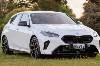 Front three-quarter view of a white BMW M135i parked on grass in a New Zealand setting
