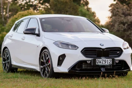 Front three-quarter view of a white BMW M135i parked on grass in a New Zealand setting