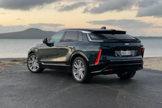 Rear three-quarter view of the Cadillac Lyriq parked by the coast showing LED tail lights and sloping roofline