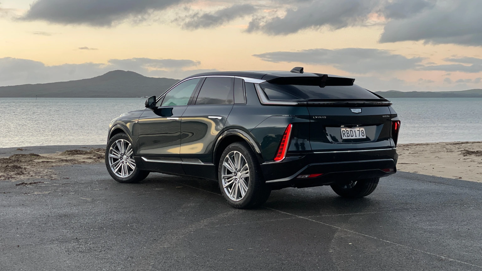 Rear three-quarter view of the Cadillac Lyriq parked by the coast showing LED tail lights and sloping roofline