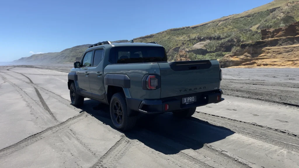 Kia Tasman X-Pro rear view driving on a sandy beach