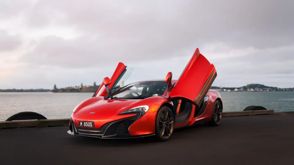 Red McLaren 650S supercar with dihedral doors open parked by the waterfront