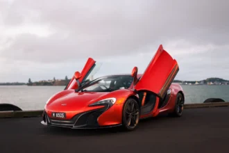 Red McLaren 650S supercar with dihedral doors open parked by the waterfront