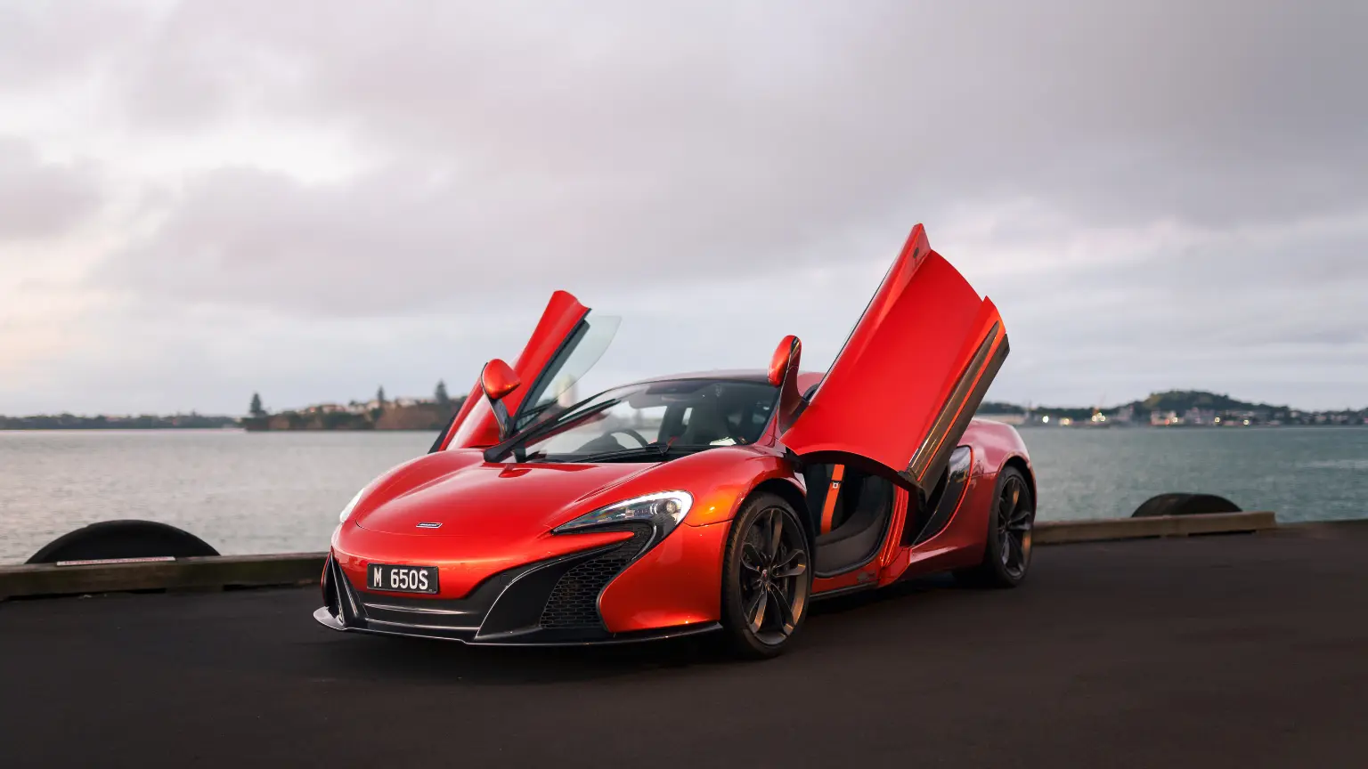 Red McLaren 650S supercar with dihedral doors open parked by the waterfront