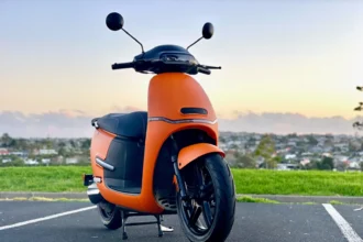Orange electric scooter front view parked on a road with city background at sunset