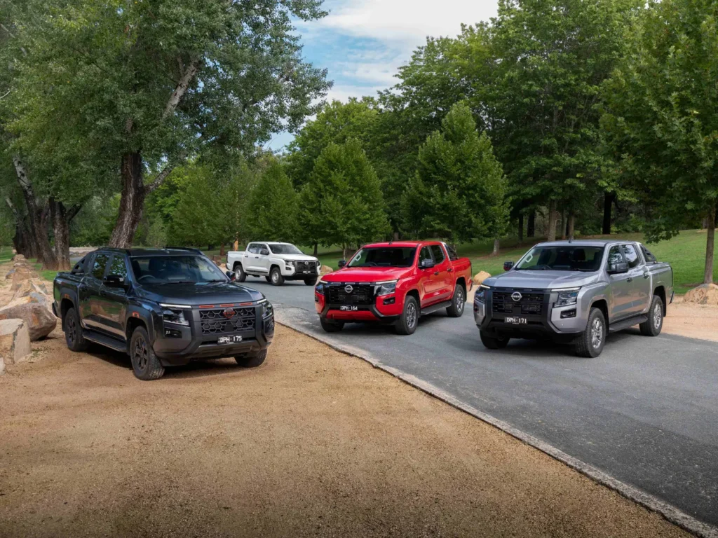 2026 Nissan Navara lineup parked on a scenic road with trees, showing black, red, silver, and white pickup trucks
