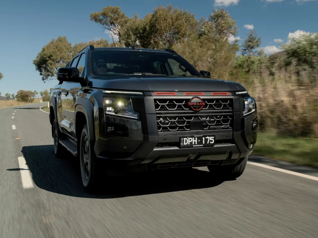 Front view of black 2026 Nissan Navara driving on an open road with headlights on