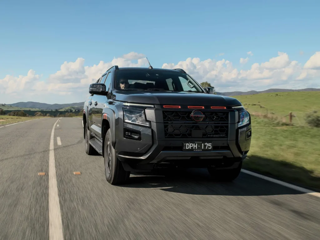 2026 Nissan Navara pickup truck driving on a rural highway with mountains and blue sky in background