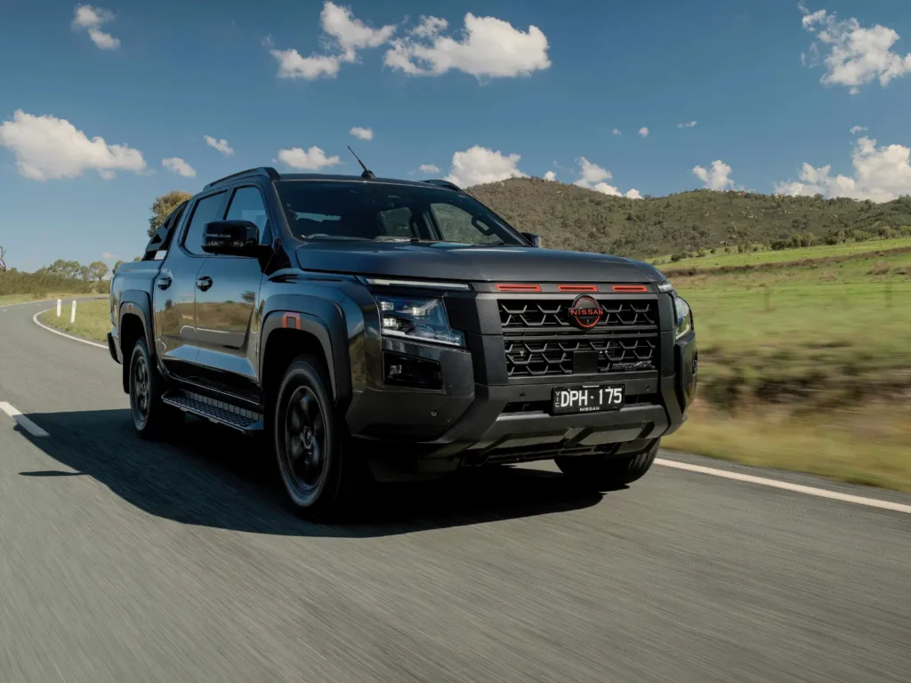 Black 2026 Nissan Navara driving on a country road with hills and clear sky