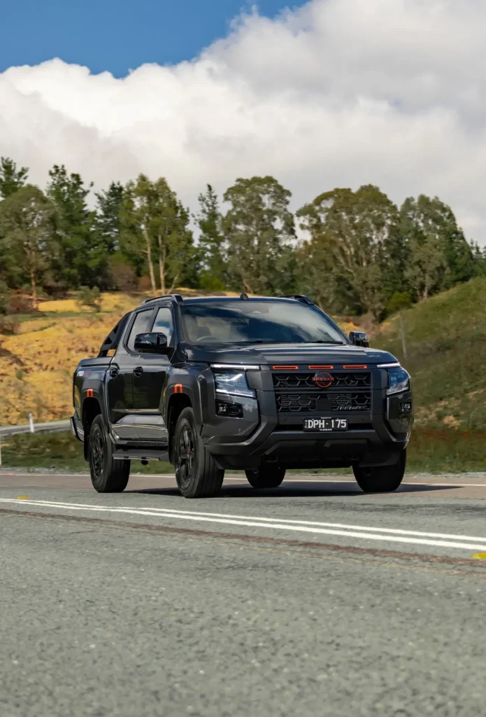 Black 2026 Nissan Navara driving on a curved road with countryside landscape