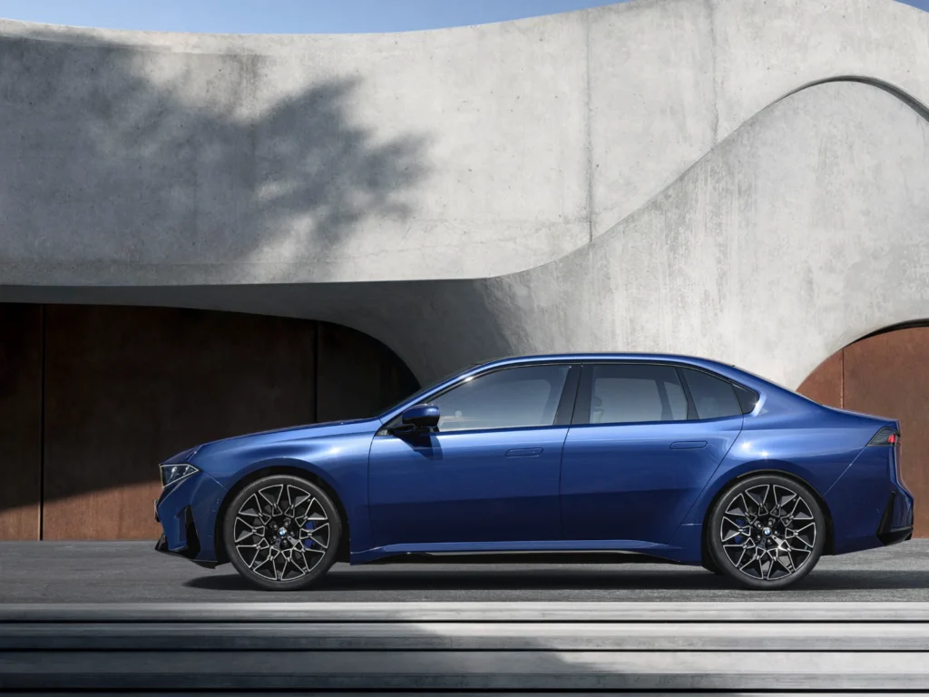 BMW i3 fully electric sedan side profile in metallic blue parked against a modern architectural backdrop