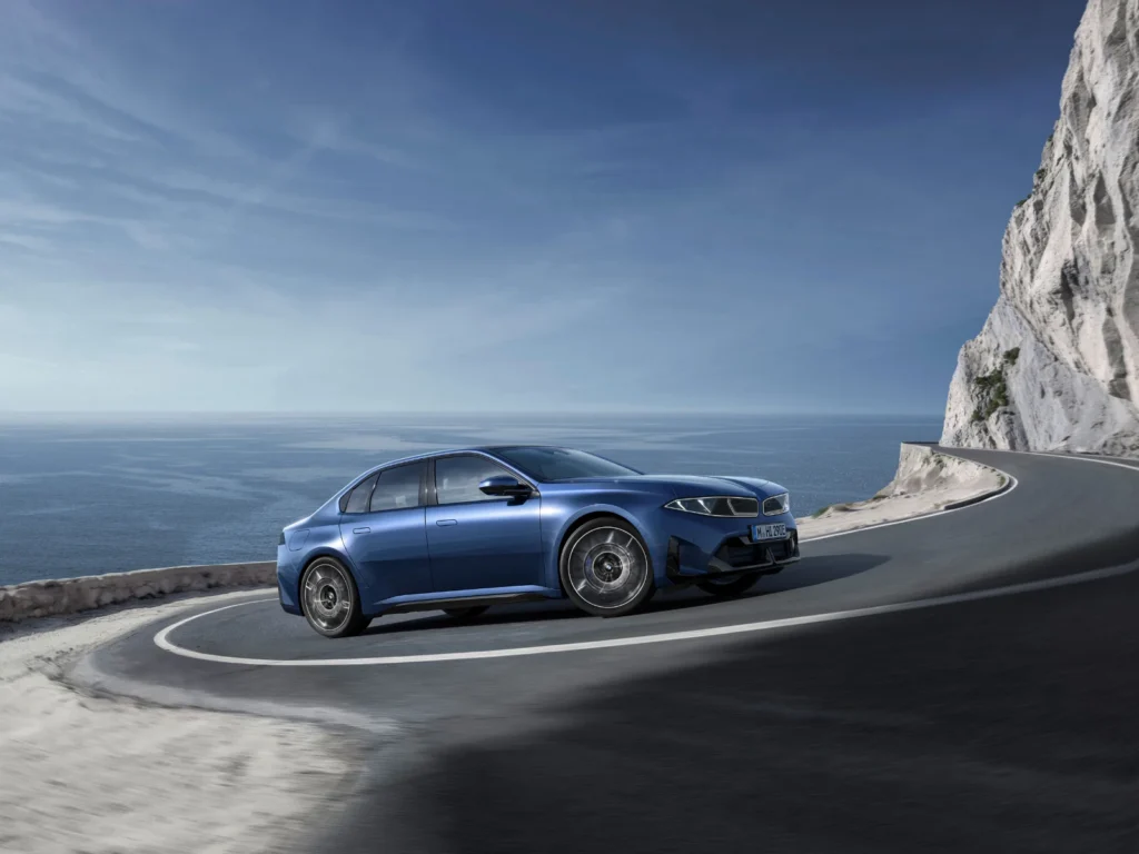 BMW i3 electric sedan in blue driving on a winding coastal cliff road with ocean views