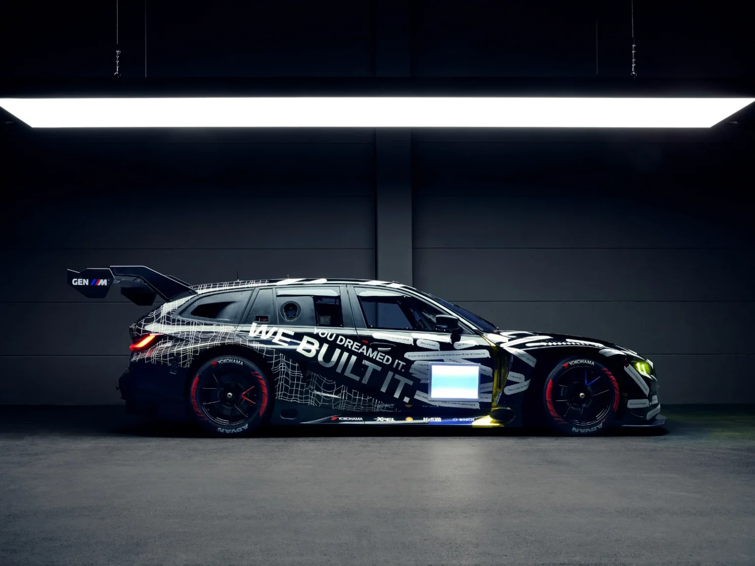 BMW M3 Touring race car side view in a studio with “We Built It” livery and large rear wing