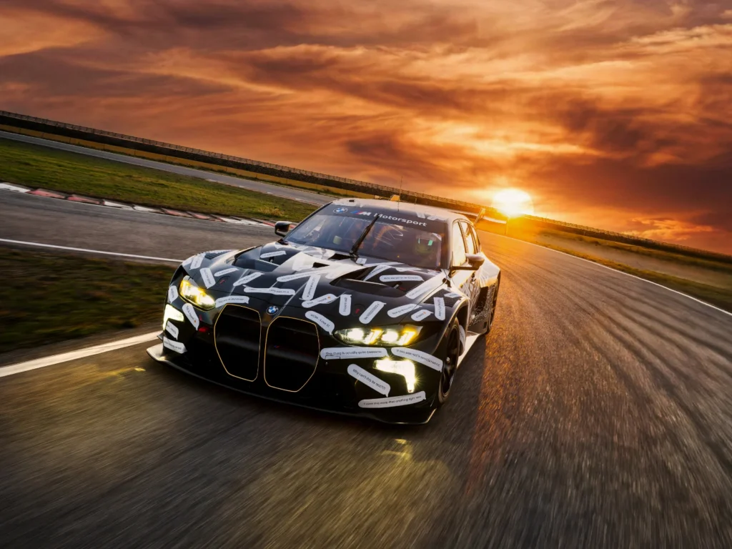 BMW M3 Touring race car driving on race track at sunset with headlights on