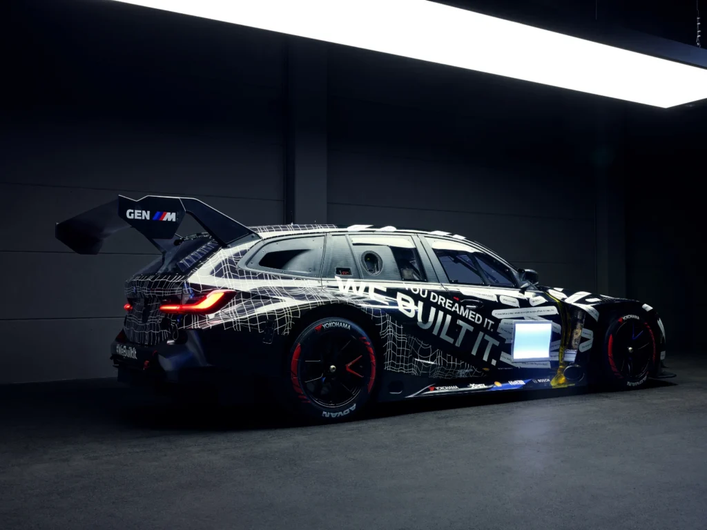 Rear side view of BMW M3 Touring race car with Gen M branding and aerodynamic wing in dark studio