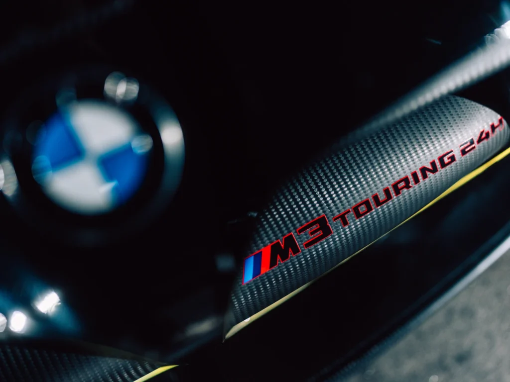 Close-up of BMW M3 Touring badge on carbon fiber surface with M3 Touring 24h text