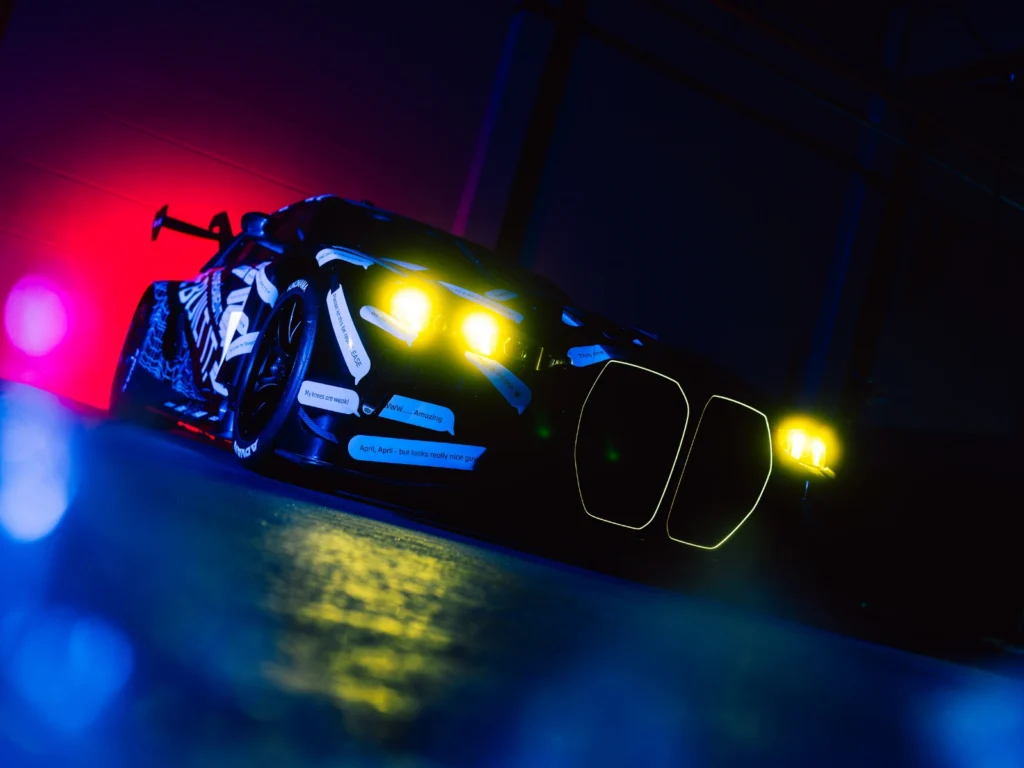 BMW M3 Touring race car front angle with yellow headlights and neon lighting in studio