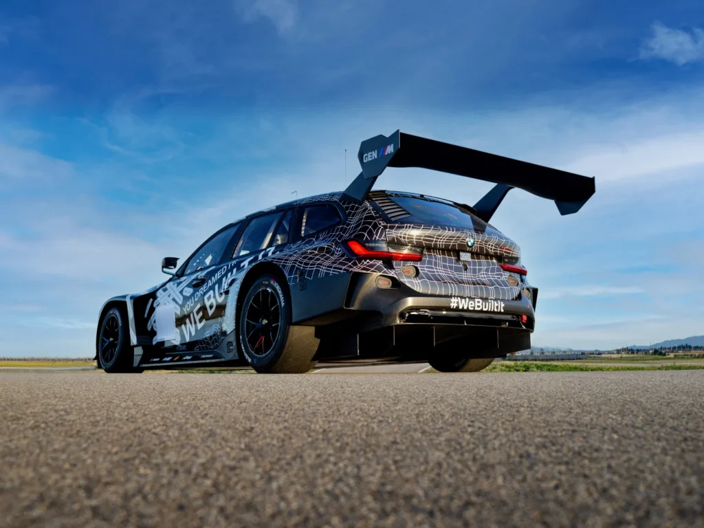 Rear angle of BMW M3 Touring race car parked on track showing large rear wing and diffuser