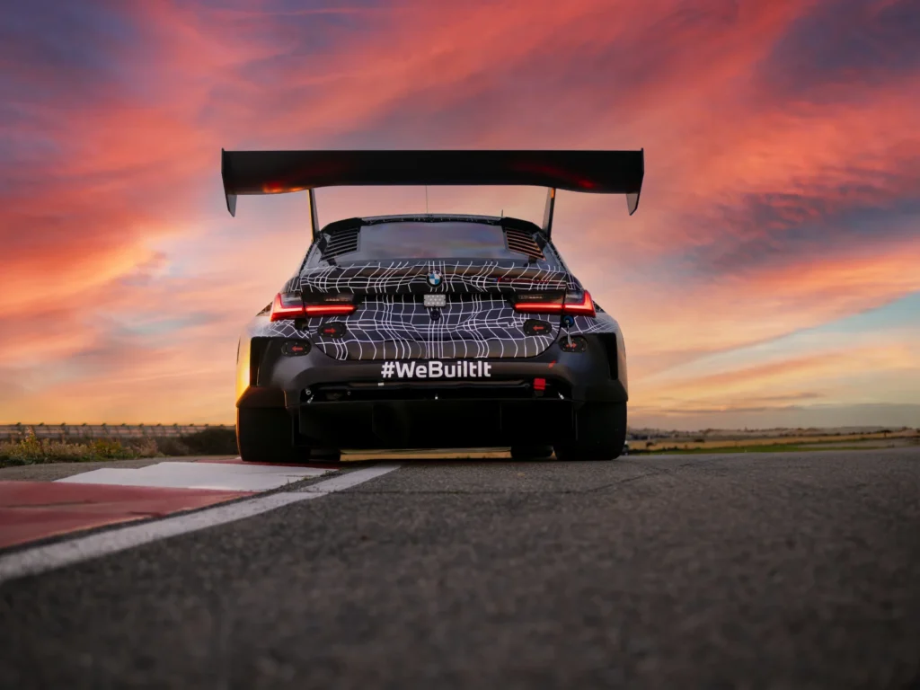 Rear view of BMW M3 Touring race car with “WeBuiltIt” text at sunset on race track