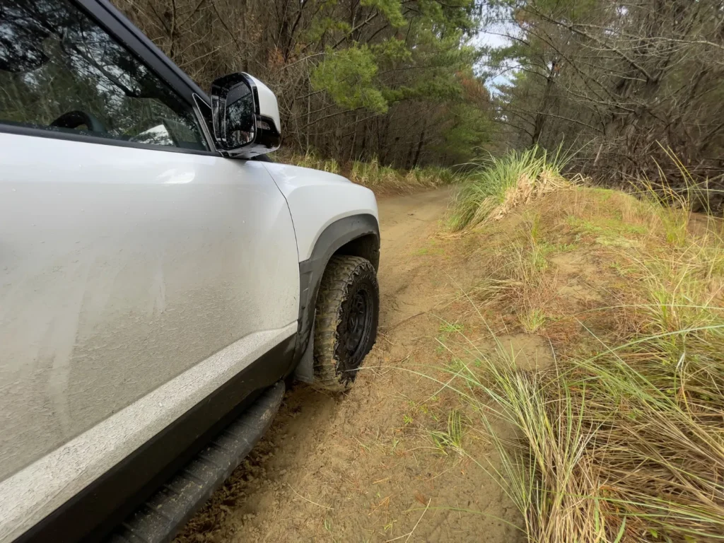 BYD Shark 6 driving through muddy off-road trail side angle